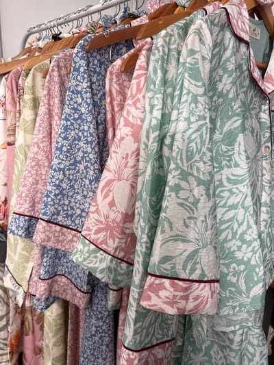The image depicts a stack of pajamas, likely folded, on hangers, in what appears to be a retail setting. The pajamas are various colors and floral patterns, including green, pink, and blue. A "Sleepin" tag is visible on one of the pajama tops. The background appears to be a retail or storage area with a plain wall. There is no information about the location being in Chorrillos, Peru.