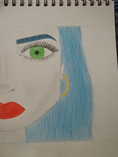 This image displays a colored pencil drawing of a stylized female face, situated on a white page within a spiral-bound sketchbook. This scene is located in 서대문구, South Korea. The drawing portrays the right side of a face, featuring a large, almond-shaped right eye with a bright green iris, a black pupil, and long black eyelashes on both lids. An arched, dark blue eyebrow is positioned above the eye. The right contour of a nose bridge is faintly visible. In the lower-left portion of the drawing, full red lips are depicted. Light blue hair flows vertically down the right side of the face, partially obscuring a gold-colored hoop earring on the right earlobe. The skin areas of the face are largely uncolored, allowing the white paper to show through, with subtle shading present. The drawing utilizes visible colored pencil strokes. The black spiral binding of the sketchbook is present along the top edge of the page, and the sketchbook itself rests on an unidentifiable dark, textured surface.