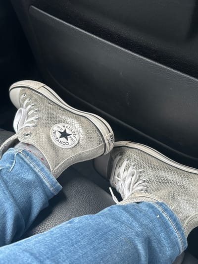 The image shows a pair of silver, high-top Converse All-Star sneakers being worn inside a vehicle. The person wearing the sneakers is also wearing blue jeans and gray socks. The interior of the vehicle appears to be black. There is no information in the image to confirm this is South Ockendon, United Kingdom.