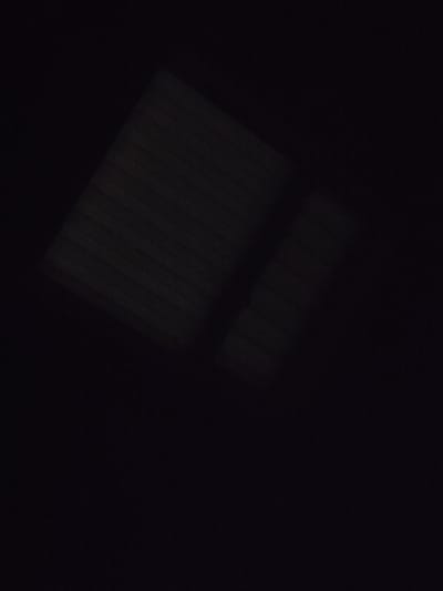 The image is a very dark, close-up shot of a ribbed surface that appears to be black fabric or a similar material. There are subtle reflections on the surface, suggesting it is somewhat glossy or has a sheen. The lighting is minimal, with some areas appearing brighter due to highlights reflecting off the ridges of the material. The background is entirely black, with no discernible features or context. There are no people, animals, or any recognizable objects within the frame. The image does not provide any information about its location in Shkurupiivka, Ukraine.