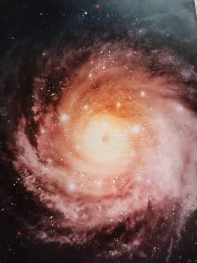 This is an image of a spiral galaxy with a bright, luminous core. The galaxy is depicted with swirling arms of dust and stars, rendered in shades of pink, orange, and yellow, set against a dark, star-filled background. There are no people, objects, actions, interactions, or environmental details related to the city of Ötegen batyr, Kazakhstan, visible in this image.