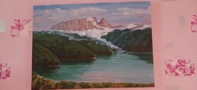 The image shows a painting of a serene mountain landscape with a lake. The painting is hung on a pink, textured wallpaper with floral print accents. The painting depicts a body of water reflecting the sky, surrounded by lush green hills. In the background, majestic mountains with snow-capped peaks rise against a cloudy sky. The painting's style is impressionistic, with visible brushstrokes that add texture and depth to the scene. There are no people or animals visible in the painting or the room. The overall impression is one of natural beauty and tranquility. The location within Ganja City, Azerbaijan is not specified in the image.
