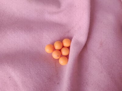 This image shows a cluster of seven small, round, orange objects, possibly marbles or small candies, arranged on a pink, textured fabric. The fabric appears to be a woven material with a subtle diagonal pattern. The objects are clustered together, with some overlapping. The lighting is soft, casting gentle shadows. There is no indication of location within the city of Inhulo-Kamianka, Ukraine.