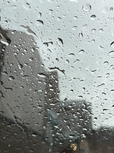 The image shows raindrops on a window, blurring the view outside. The background appears to be an urban scene, with indistinct buildings visible through the rain-streaked glass. The exact location within Durham, United Kingdom is indeterminate from this image alone. There are no people visible, and the focus is on the water droplets and the obscured view beyond the window.