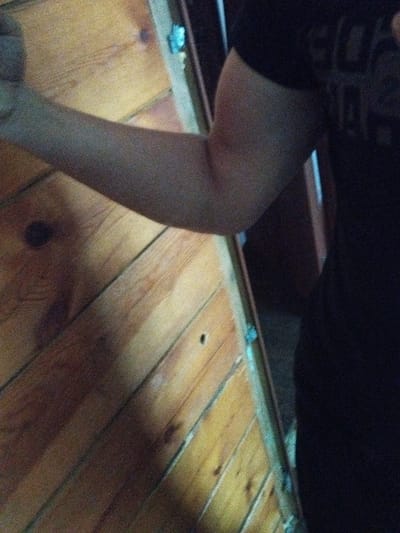 The image shows a close-up of a person's arm, which appears to be resting against a wooden surface. The wooden surface is made of planks and has a diagonal grain pattern. The lighting in the image is dim, creating shadows on the wooden surface. The person's arm is smooth and appears to be uninjured. There are no visible details that would indicate the location in Kirensk, Russia.