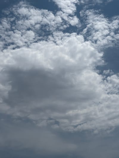 The image is an aerial view of a cloudy sky over Grapevine, United States of America. The sky is filled with various types of clouds, ranging from light and wispy cumulus clouds to darker, more substantial storm clouds. The clouds are illuminated by sunlight, creating a dynamic interplay of light and shadow. The overall impression is one of a vast and ever-changing sky. There are no people, subjects, or objects visible in the image. The environment is purely the sky.