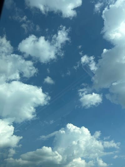 The image depicts a bright, sunny day with a deep blue sky filled with fluffy white clouds. The scene is an outdoor view looking upwards, likely from the ground or a low elevation. Sunlight filters through the clouds, creating varying degrees of brightness and casting soft shadows. In the distance, faint, parallel lines are visible across the sky, possibly indicating airplane contrails or reflections. The clouds themselves are varied in size and density, with some appearing wispy and others more substantial. The overall impression is one of a beautiful, clear day with fair weather conditions. No people or man-made objects are clearly discernible in the scene, apart from the possibility of contrails. The time of day appears to be midday or early afternoon due to the bright light. The location context of Verinsko, Bulgaria, does not offer specific visual cues within the image itself, but suggests a terrestrial setting. There is no visible text.