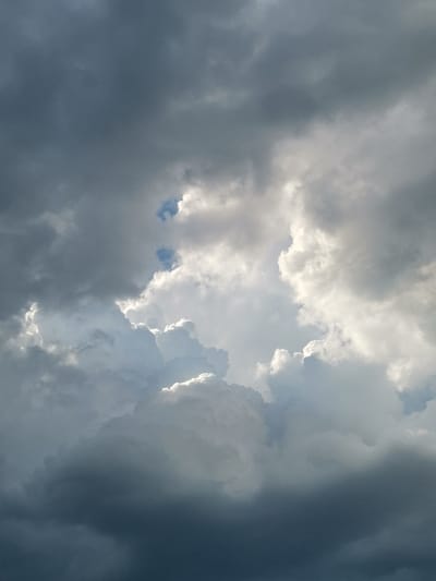The image shows a dramatic sky with a mix of dark, heavy storm clouds and bright, sunlit clouds. There are patches of blue sky visible through breaks in the clouds, particularly in the upper portion of the image. The lighting suggests that the sun is behind some of the clouds, creating highlights and shadows. The overall impression is one of an approaching or passing storm. The image does not contain any people, subjects, objects, actions, or interactions. It is a purely natural scene of the sky.
