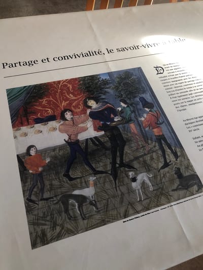 The image shows a poster, with the text "Partage et convivialité, le savoir-vivre à table" printed prominently on the left. The poster features a reproduction of a medieval painting showing a group of people sitting at a table and dining, with several dogs around them. The text to the right of the image appears to discuss table manners in the Middle Ages. The bottom of the poster includes the title of the artwork "Mort de Gaston Phébus, comte de Foix / Jean Froissart, Chroniques, XVe siècle, Paris, Bibliothèque nationale de France, Français 2646, f. 12."
The location of the image isn't Veytaux, Switzerland, but rather references medieval table manners according to historic French documents, and the image shown on the poster is housed at the Bibliothèque nationale de France in Paris.