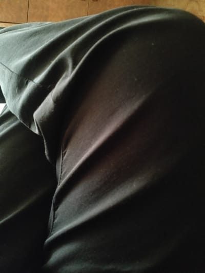 The image shows a close-up, abstract view of dark fabric, likely clothing, with visible folds and textures. The fabric appears to be made of a soft material, possibly cotton or a blend, and is a deep, solid color. The lighting creates shadows and highlights that emphasize the contours and draping of the material. There are subtle variations in tone, suggesting that the fabric might be slightly worn or have a matte finish. The background is out of focus but appears to be a warm, neutral color, possibly wood paneling or a similar surface.

The composition is primarily focused on the fabric itself, with no distinct subjects like people or recognizable objects. The activity or event taking place is not evident from the image; it is a still shot that captures the texture and form of the material. Notable details are limited to the visual characteristics of the fabric, such as its color, texture, and the way it is folded. There are no discernible cues related to time of day, weather, or specific location. The image does not evoke any strong emotions due to the lack of context and identifiable elements. No visible text is present in the image.