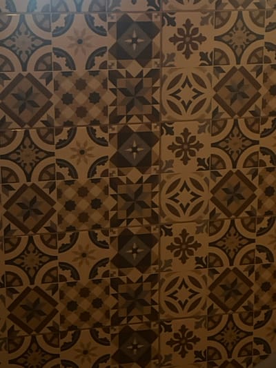 The image showcases a patterned tile floor with an array of geometric and floral designs. The tiles alternate between light and dark shades of brown, creating a visually engaging mosaic. The patterns include star motifs, stylized floral elements, and intricate geometric arrangements. The tiles are arranged in a grid-like fashion, filling the frame with a harmonious and decorative surface.