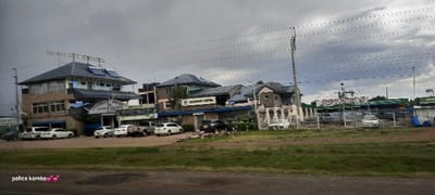 Leadway Hotel and Standard Motors are featured under a cloudy sky. A two-story building houses Leadway Hotel, adorned with solar panels on its roof. Several parked vehicles are in front of it. Adjacent, Standard Motors has a fenced area with what appear to be several vehicles inside. Power lines stretch across the sky. The foreground has vegetation, likely along a roadside. The inscription "police komba" with heart emojis is visible in the bottom left.