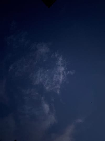 The image depicts a night sky. There are clouds scattered throughout. A single, bright celestial object (likely a star) is visible. The overall color palette is dominated by shades of dark blue. No people, subjects, objects, actions, or interactions are discernable in the image. There is no indication this image was taken in Manole, Bulgaria.