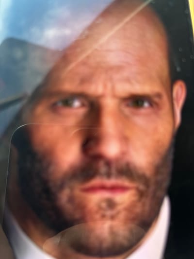 This is a close-up, out-of-focus photograph of a man's face. The man has fair skin, a receding hairline, and a beard. He is wearing a white collared shirt and a dark jacket. The lighting in the image is harsh, creating strong highlights and shadows. There are reflections on the surface of the image, possibly from a protective covering or glass. The background is dark and indistinct. There is no discernible information about the location being Severynivka, Ukraine.