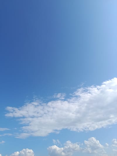 The image shows a clear blue sky with scattered white clouds. The clouds are predominantly in the lower right portion of the frame, with some appearing higher and more wispy. The sky is a vibrant blue, suggesting a sunny day. There are no visible people, buildings, or other objects in the image. The scene is a natural outdoor environment.