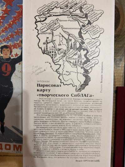 The image contains a map with text, likely a newspaper clipping, displaying a hand-drawn map of a region in Russia. The map highlights various cities and towns, including "Анжеро-Судженск", "Мариинск", "Тайга", "КЕМЕРОВО", "Новоивановка", "Межреченск", and "Суслово". Locations are labeled with professions like "Художник", "Артист", "Режиссёр", "Поэт", "Философ", and "Писатель", followed by names. Some areas are depicted with industrial elements like cranes. The text describes a "карту «творческого СибЛАГа»" (map of the "creative SibLAGa"). The clipping also mentions "Кузбасс", "СибЛАГ", and specific dates like "1939 года". There is also a handwritten inscription at the top left corner which appears to be in Russian. The lower right corner of the clipping has a byline that reads "Рисунок Валерия Андрианова." (Drawing by Valery Andrianov). The overall setting is a printed document with handwritten additions. The image does not depict the city of Ust'-Pyzas.