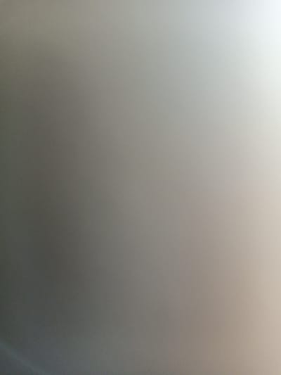 The image is a blurred, abstract photograph of a surface that appears to be a wall or a screen. There are no discernible objects, people, or actions. The lighting suggests a gradient from darker tones on the left to brighter tones on the right, indicating a light source from the right side of the frame. The image provides no information about the city of Romodan, Ukraine, or any specific location within it.