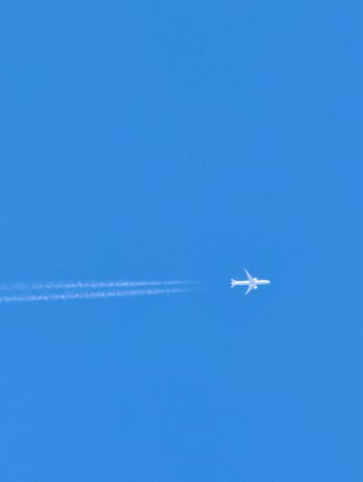 An airplane is flying across a clear blue sky, leaving a white contrail behind it. The plane is white and has its wings extended horizontally. The contrail is faint and wispy, suggesting that the airplane is at a high altitude. The sky is a uniform bright blue, indicating a sunny day with good visibility. There are no clouds visible in the image. The scene is serene and devoid of any other objects or people. The image appears to be taken during the daytime, given the brightness of the sky. The perspective suggests the photo was taken from the ground looking upwards. There is no visible text in the image.