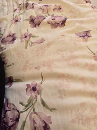 The image shows a close-up view of a fabric with a floral pattern. The pattern consists of purple and pink flowers, possibly tulips, with green stems and leaves, set against a light-colored background. The fabric appears to be wrinkled and creased, suggesting it might be a bedsheet, curtain, or garment. There are no people or specific environmental details visible that would indicate a location in Avtury, Russia, or any other city.