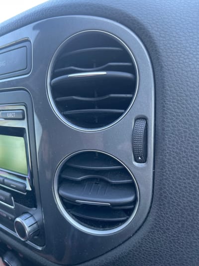 The image shows a close-up view of the interior of a car's dashboard, specifically focusing on a dual air vent and a part of the car's infotainment system. The air vents are circular with horizontal slats. To the left of the vents, a silver button labeled "EJECT" is visible above a screen. Below the screen, a rotary dial with silver accents is present. The dashboard is made of dark, textured material, likely plastic or leather. The lighting suggests an indoor or shaded environment, typical of a car interior. No people are visible in the image. The location of Novaky, Ukraine, is not identifiable from the visual elements in the image.