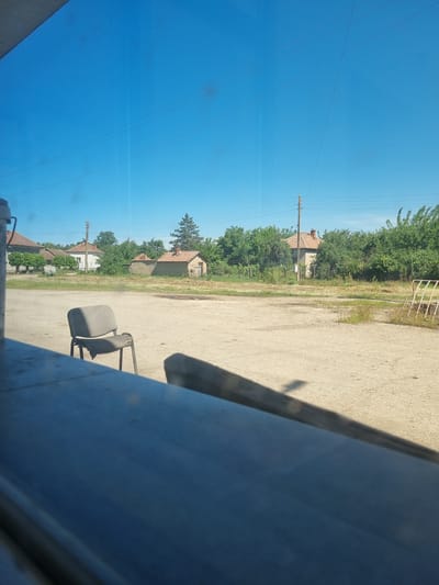 A scene in Glava, Bulgaria, presents a clear blue sky contrasted with a ground level view of buildings and trees. Overhead power lines stretch across the sky. A vacant office chair stands on a concrete surface, near an obstruction from the right side.