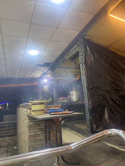Inside a smoke-filled restaurant, a person works near a large cylindrical container. The space is covered by a black tarp overhead, supported by a steel frame. The interior walls are tiled, and a stainless steel handrail is visible in the foreground. The ambiance suggests an industrial or commercial setting.