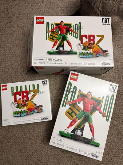 The image shows three LEGO sets featuring Cristiano Ronaldo. The largest set, on top, is a "Cristiano Ronaldo-CR7 Collectors Set" with 1344 pieces. To the left, a smaller set is labeled "Cristiano Ronaldo - Soccer Highlights" with 490 pieces. On the right, another set is titled "Cristiano Ronaldo - Soccer Legend" with 854 pieces. All sets are new in their original packaging and are placed on a carpeted floor. The lighting suggests an indoor setting. The image does not provide any information about the location in Ephrata, United States of America.
