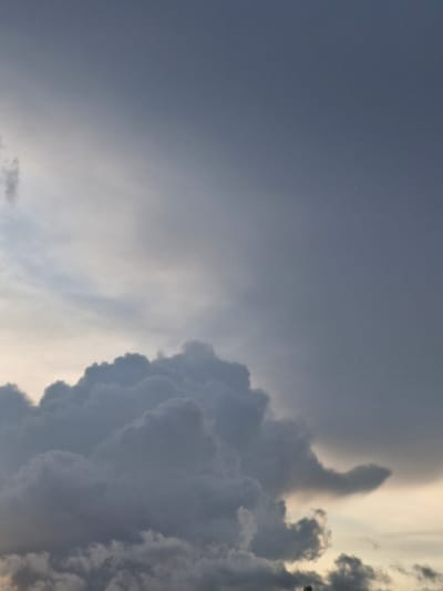 The image captures a cloudy sky over Saulgoži, Latvia. The clouds are dark and heavy, suggesting impending rain or a storm. The sky is a mix of grays and blues, with a hint of pale yellow near the horizon. There are no people, subjects, or objects visible in the frame, as the image is focused solely on the atmospheric conditions. The environment is characterized by a vast expanse of sky filled with dramatic cloud formations.