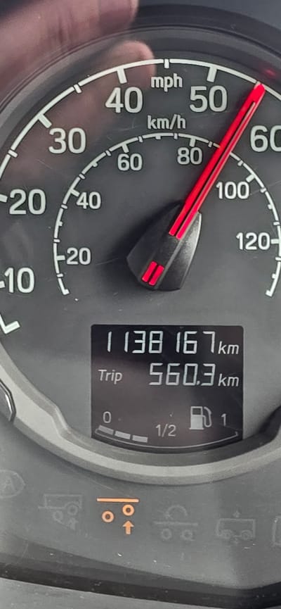 The image shows a close-up of a car's dashboard, specifically the speedometer and a digital display. The speedometer shows a speed of approximately 50 mph, with the needle pointing slightly above the 50 mph mark. The digital display shows the odometer reading as 1138167 km and the trip meter as 560.3 km. Below these readings, there is a fuel gauge showing the fuel level at approximately 1/2. There are also various indicator lights visible on the dashboard, including a symbol that appears to represent parking sensors or a similar vehicle assistance system. The dashboard is dark gray in color, and the lights on the speedometer are white. The overall impression is that this is a photograph taken inside a vehicle, likely while it is in operation. There is no information in the image to indicate the location in the city of Newark and Sherwood, United Kingdom.