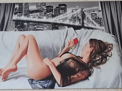 The image is a painting depicting a woman lying on a white sofa. She is wearing a black lace garment and holding a red rose. The background shows a nighttime city skyline with a bridge, likely New York City, given the presence of the Brooklyn Bridge. The painting is detailed and realistic, with a focus on the woman's form and the textures of the fabric and cityscape. There is no indication that this scene is located in Atkarsk, Russia; the urban background strongly suggests an American city.