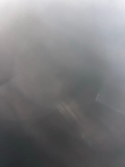 The image shows a blurry, out-of-focus background that transitions from a brighter, almost white area on the left to a darker, muted gray on the right. There are vague streaks of lighter tones within the darker portion, hinting at possible light reflections or textures that are not clearly defined due to the lack of focus. The overall impression is soft and indistinct, lacking clear subjects or details.