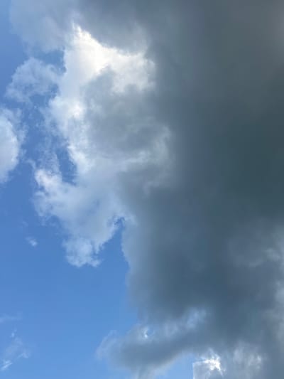 The image shows a dramatic sky with a clear division between bright blue sky and dark, heavy storm clouds. The sun is partially obscured by these clouds, creating a bright, almost white area where the light is most intense. To the left, lighter, fluffy clouds drift across the blue expanse. The overall impression is of an impending or ongoing storm. The location is identified as Beryozovka, Russia. There are no people, objects, or actions depicted in the image.