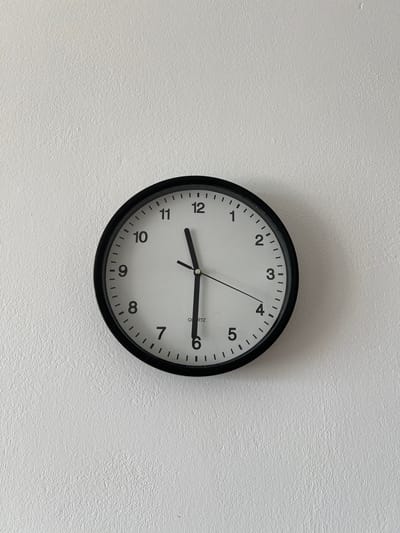The image shows a black-framed analog clock with a white face hanging on a textured white wall. The clock has black Arabic numerals and thin black hour and minute hands. The hour hand is pointing slightly past the 11, and the minute hand is pointing at the 5. The clock displays the time as approximately 11:25. The wall appears to be an interior wall, possibly in a home or office. There are no people or other objects visible in the frame. The image composition is centered on the clock. The lighting is even, suggesting it was taken in daylight or with artificial lighting.

The provided location of Kobylnica, Poland, is not visually verifiable from the image content.