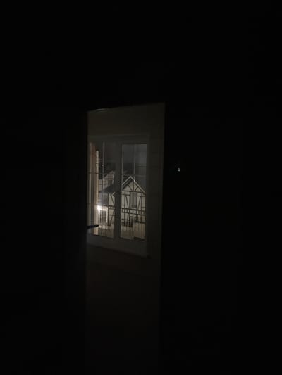 The image shows a night scene with a view through a window. Outside the window, there is a structure that appears to be scaffolding or some type of metal framework. Inside, the room is dark, but the light from outside illuminates the window frame. Based on the location provided, this scene is likely in Хлябово, Russia.