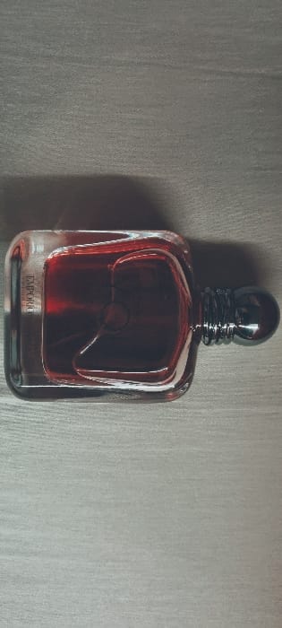 The image shows a bottle of Emporio Armani cologne on a white surface. The bottle is rectangular with a silver top and a dark red liquid inside. The bottle is sitting on a white surface that appears to be a countertop. The coordinates provided are for a location in Puna'auia, French Polynesia, but the image does not provide any information about the location. There is no indication of any people or actions in the image.