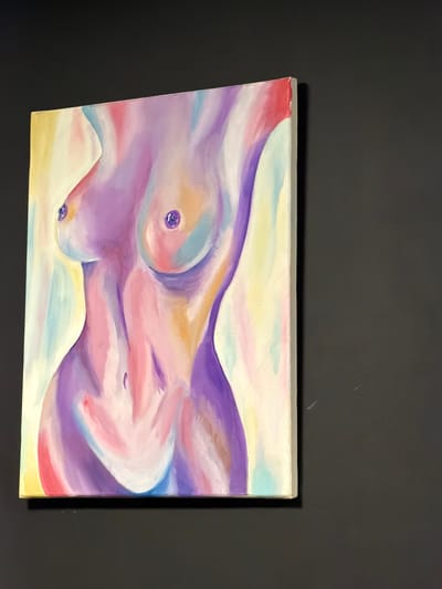 The image is a photograph of a painting displayed on a dark, textured wall. The painting, which is landscape-oriented, depicts an abstract representation of a nude human torso. The artist has used a soft, pastel color palette, with dominant hues of lavender, pink, yellow, and light blue. The figure is rendered in smooth, flowing lines, suggesting curves and contours of the body without sharp details. The painting appears to be an oil or acrylic on canvas, with visible brushstrokes contributing to the soft, blended effect. The overall mood conveyed by the artwork is gentle and serene. There is no discernible text in the image, nor are there any explicit cues about the time of day, weather, or specific location within Stryi, Ukraine, beyond the artwork itself being the primary subject. The presentation suggests the painting is an art piece being showcased, possibly in a home or gallery setting.