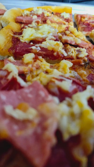The image shows a close-up view of a pizza. The pizza appears to have a variety of toppings, including what looks like sliced salami or pepperoni, and scrambled eggs. The crust is golden brown and appears to be slightly puffy. The lighting is warm, suggesting it might be taken indoors with artificial light, possibly in a kitchen or dining area. The overall impression is of a hearty and appetizing dish. There are no people, text, or distinct location cues visible in the image that would specifically link it to Kaka, Turkmenistan, other than the provided metadata. The focus is entirely on the texture and colors of the pizza toppings and crust.