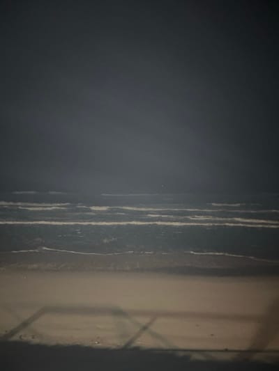 A close-up shot features a textured, dark gray wall on the left and a lighter, smoother surface on the right. Vertical white lines streak down the gray wall. On the right, a faint shadow suggests a window or geometric structure. The lighting is subdued, creating a moody and abstract composition.