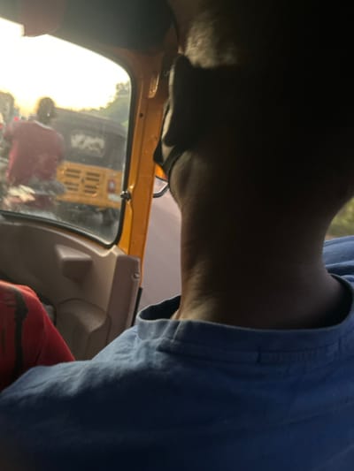 An indoor shot with part of a person's face, head, and upper body angled downwards. The person wears a blue shirt. A yellow vehicle interior frames the scene, with the outside world visible through the window, showing a blurred street scene and part of a yellow vehicle. The light is bright and diffused, creating strong shadows on the person's face and neck.