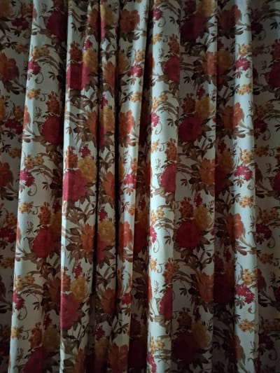 The image shows a close-up of folded fabric. The fabric has a floral pattern featuring red, orange, and yellow flowers with brown leaves against a light background. The folds create a repeating horizontal pattern. The image provides no information regarding the location in Krumovgrad, Bulgaria or any people, subjects, objects, actions, interactions, or environment beyond the fabric itself.