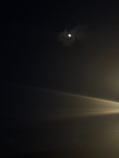 A nighttime scene depicts a faint moon partially obscured by clouds in the upper left. To the right, streaks of light emanate downwards, possibly from a light source outside the frame. Vertical lines are visible on the right, possibly wires or cables. The scene is predominantly dark, obscuring any further details about location or objects. No people are visible. There is no evidence in the image to confirm the location is Borino, Bulgaria.