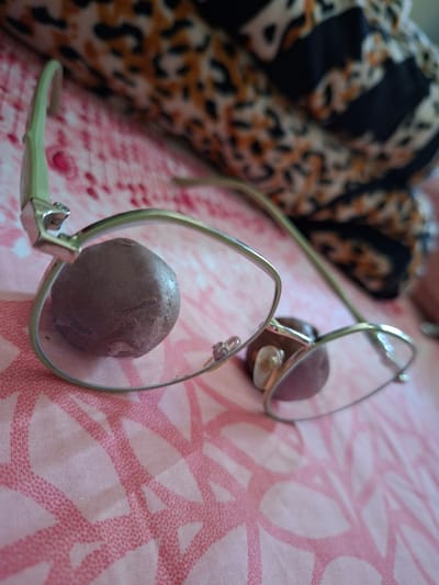 The image depicts a pair of glasses lying on a pink patterned cloth, with a dark chocolate truffle in each lens. To the left of the glasses is a leopard-print fabric. There is no information about the location of Pie, Indonesia, or any other indication of the scene's location.