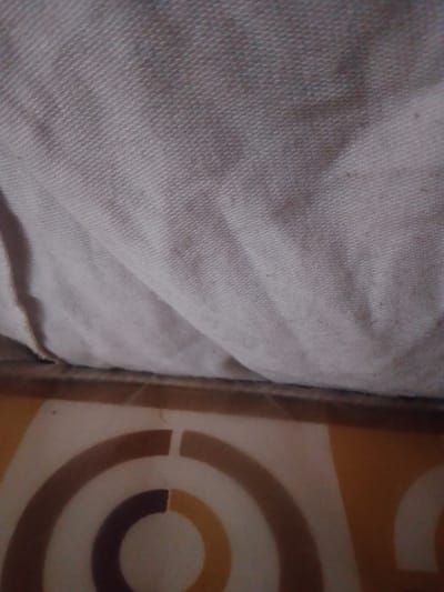 The image shows a close-up view of fabric draped over a surface with a patterned design. The fabric is a light color and appears to be textured. Below the fabric, there is a surface with a design composed of concentric circles in shades of brown and beige. The image provides no indication of its location in Panhauya, Nigeria, or any other specific place. There is no information about people, subjects, objects, actions, or interactions. The environment is limited to the visible fabric and patterned surface.