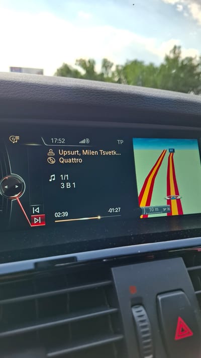 The image displays a car's infotainment system screen, showing navigation and music playback information. The navigation map on the right shows a road with red and yellow lane markers. The music interface on the left displays "Upsurt, Milen Tsvetkov... Quattro" as the song title and artist. It also shows "1/1 3 B 1" which could be track or album information, and a progress bar indicating 02:39 into the track with a total of -01:27 remaining. The time displayed is 17:52. The car appears to be on a road, with a cloudy sky and trees visible through the windshield, suggesting an outdoor, daytime setting. There are no people visible in the image, only the car's internal display and controls. The location is identified as Malo Konare, Bulgaria.