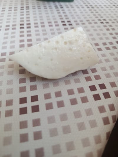 A close-up, slightly blurry photograph shows a white, somewhat amorphous object, possibly food, resting on a beige and white checkered surface. The object has a slightly irregular shape with rounded edges and appears to have small indentations or bubbles on its surface. The background surface is a fabric with a pattern of small squares, alternating between a lighter beige and a darker brown color, arranged in a grid. The lighting appears to be from above. The specific location in the city of Cupcini, Moldova, cannot be determined from the visual information provided in the image.