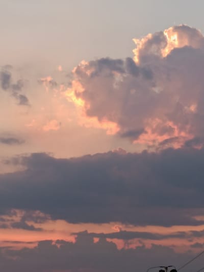 The image shows a sky with clouds at sunset. The clouds are lit with warm colors of orange and pink, with some darker gray clouds visible. The scene is an outdoor environment with no specific buildings or landmarks identified, though it is noted as being in Lozova, Ukraine. There are no people or any discernible actions or interactions captured in the frame. The overall atmosphere suggests a peaceful evening sky.
