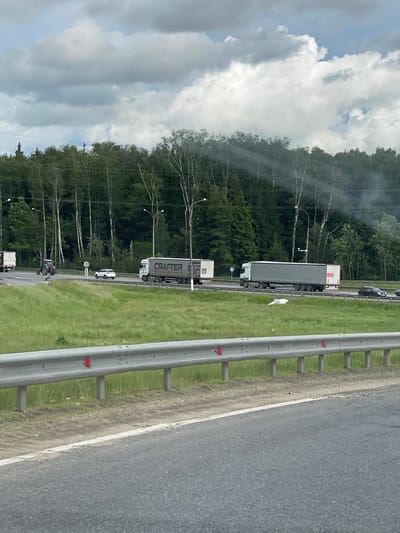 The image depicts a highway scene, likely taken from a moving vehicle. The location is identified as Starokurovo, Russia. Visible elements include:

*   **Vehicles:** A line of trucks and cars are present on the highway. One prominently displays "CRAFTER" lettering on its side.
*   **Roadside:** A metal guardrail lines the highway. Grass and trees are visible beyond the guardrail.
*   **Environment:** The sky is cloudy.
*   **Interaction:** Vehicles moving on the highway in Starokurovo.