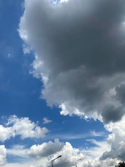 The media file captures a dynamic sky over Lopaskyne, Ukraine. The scene is dominated by a dramatic interplay of light and shadow created by various cloud formations. A large, dark gray cloud mass occupies the left side of the frame, suggesting impending rain or a storm. This is contrasted by bright, white cumulus clouds scattered across the blue sky, particularly on the right and towards the center. Wispy, cirrus-like clouds are also visible, adding texture and depth to the celestial panorama.

The orientation of the image, with the sky filling the entire frame, implies the shot was taken looking upwards from ground level. The presence of streetlights, one prominently visible on the right side of the image, along with what appears to be the top of a tree or building on the far right, provides subtle location cues, suggesting an urban or semi-urban setting.

The time of day is likely daytime, given the brightness of the sky and the illumination of the clouds. The weather appears to be mixed, with both stormy and fair-weather clouds present. This could indicate a transitional period, perhaps before or after a rain shower. No people are visible in the media file. The overall mood conveyed is one of natural grandeur and the ever-changing beauty of the sky. No text is visible in the image.