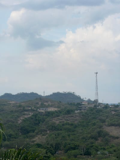 The image shows a hillside landscape with a communication tower and buildings. The sky is cloudy. It is located in the city of Gracias, Honduras.