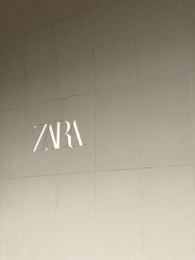 The image shows the ZARA logo illuminated on a textured, tiled wall in Qinhuai District, China. The wall is composed of square tiles with visible grout lines, and it appears to be a facade of a building. The ZARA logo is a raised, white illuminated sign, with the letters "ZARA" clearly visible and centered on the wall. The overall color scheme is neutral, with the wall being a light beige or taupe color. There are no people or other objects in the frame besides the logo and the wall. The lighting suggests it might be daytime or a well-lit exterior space.